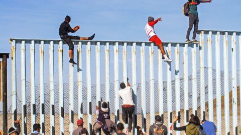 Integrantes de la caravana migrante escalan el muro fronterizo en Tijuana.