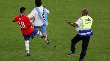 Gonzalo Jara de Chile traba a un aficionado que invadió el campo, durante el partido Chile-Uruguay de la Copa América.