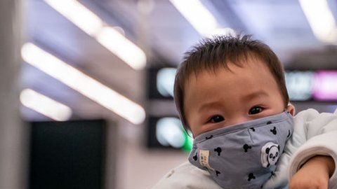 Una mujer lleva a un bebé con una máscara protectora en Hong Kong.