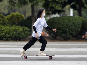 Una joven usa cubrebocas mientras monta en patineta en China.