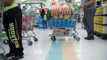 Varios clientes hacen fila con carritos de la compra en un supermercado.