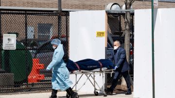 Un médico y un empleado de una funeraria transfieren un ataúd a un coche fúnebre desde una morgue temporal en NY.