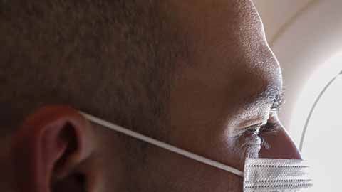 Cropped portrait of man in respirator mask flying on a plane.