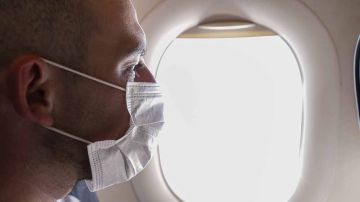 Cropped portrait of man in respirator mask flying on a plane.