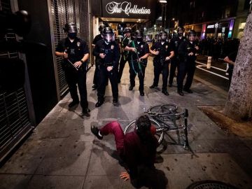 Una mujer cae de su bicicleta mientras la Policía de L.A. le bloquea el paso.