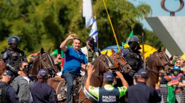 AME3374. BRASILIA (BRASIL), 31/05/2020.- El presidente de Brasil, Jair Bolsonaro, saluda a simpatizantes este domingo sobre un caballo, en Brasilia (Brasil). El presidente brasileño, Jair Bolsonaro, volvió a ignorar este domingo la gravedad de la COVID-19, que deja ya casi 30.000 muertes en el país, y asistió a una manifestación en la que hasta se paseó montado a caballo ante miles de personas. El acto se desarrolló a las puertas del Palacio presidencial de Planalto, y como ha ocurrido en manifestaciones que el "bolsonarismo" celebró los últimos domingos, hubo protestas contra el Congreso y la Corte Suprema, que según los partidarios del líder de la ultraderecha "conspiran" contra el Gobierno. EFE/ Joédson Alves