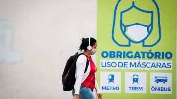 Una joven camina frente a un letrero que indica que el uso de la máscara es obligatorio en el transporte público en Sao Paulo.