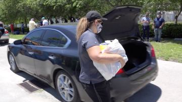 Una mujer deposita una bolsa con comida en un auto en Miami.