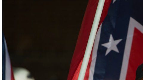 Un supremacista hace el saludo nazi con una bandera de la confederación y las cruces símbolo del Ku Klux Klan.