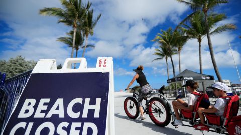 Una mujer pasando con una bicicleta frenta a un cartel de "playa cerrada" en South Beach, en Miami Beach.