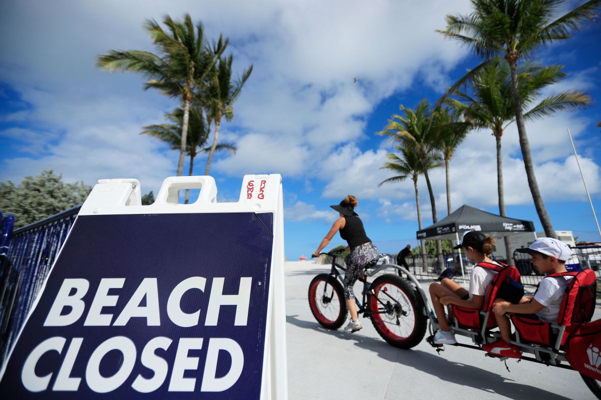 Una mujer pasando con una bicicleta frenta a un cartel de "playa cerrada" en South Beach, en Miami Beach.