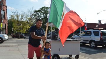 Arturo De La Rosa y su hijo con una bandera mexicana junto a su carrito ambulante en el que vende cantaritos. (Belhú Sanabria / La Raza)