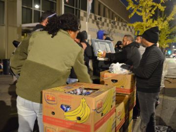Solicitantes de asilo afuera de la estación de policía del Distrito 12 reciben alimentos de voluntarios de una iglesia del barrio de Belmont Cragin. (Belhú Sanabria / La Raza)