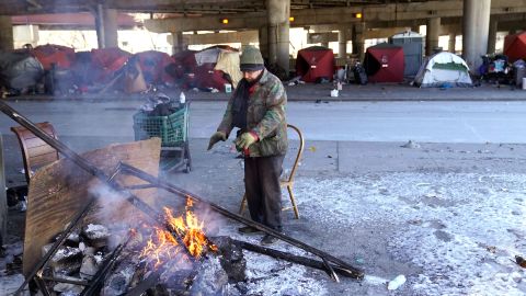 Un indigente se calienta frente a un campamento de personas sin hogar en Chicago.