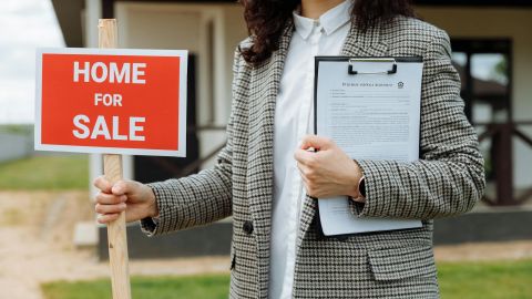 close up of a woman holding a home for sale sign